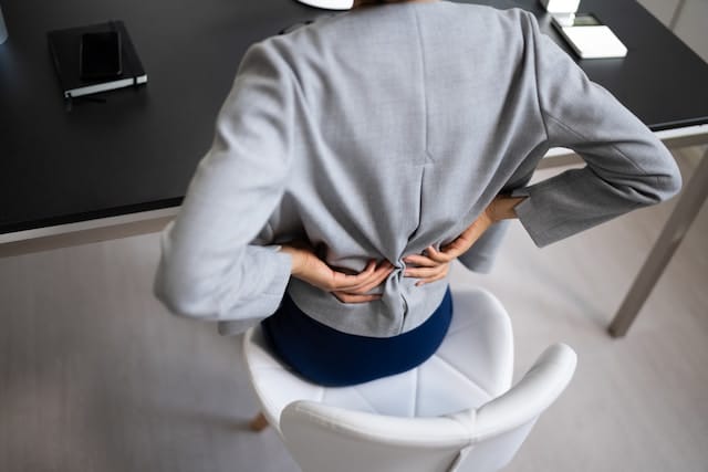 kontormedarbejder holder sig op ryggen på grund af kroniske rygsmerter